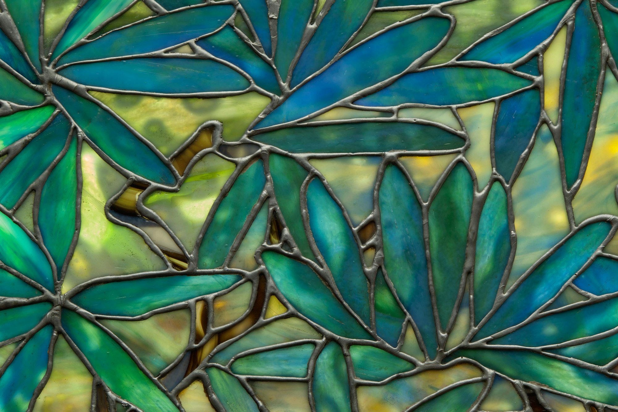 A detail of a stained glass window shows foliage: long, slender leaves in various shades of brilliant green.